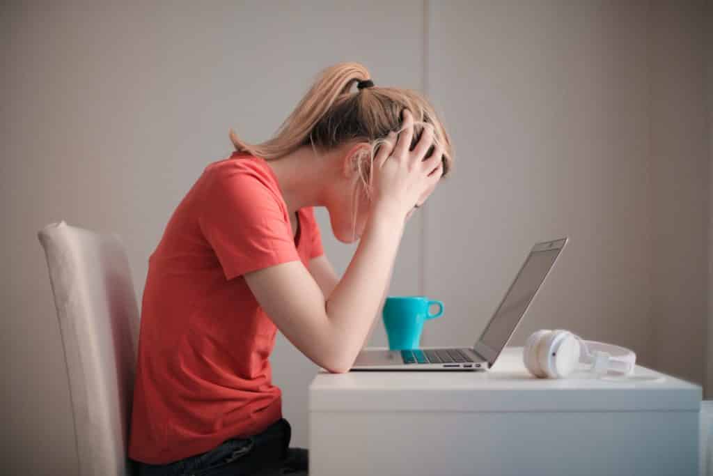 mulher exausta com as mãos na cabeça em frente do notebook